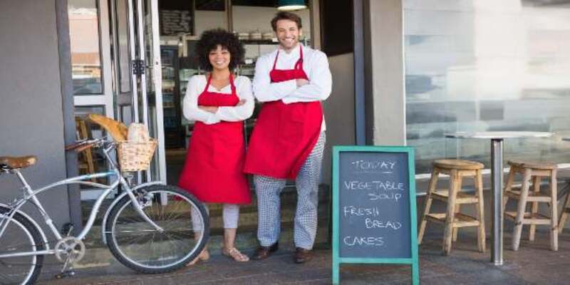 Smiling colleagues in red apron with arms crossed