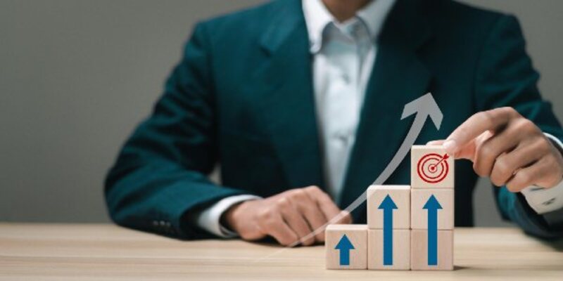 Businessman stacking wooden blocks with icon business goals and up arrow for business strategic planning