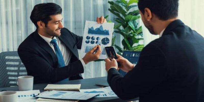 Two men in suits, one of them is holding chart and other is looking at graph