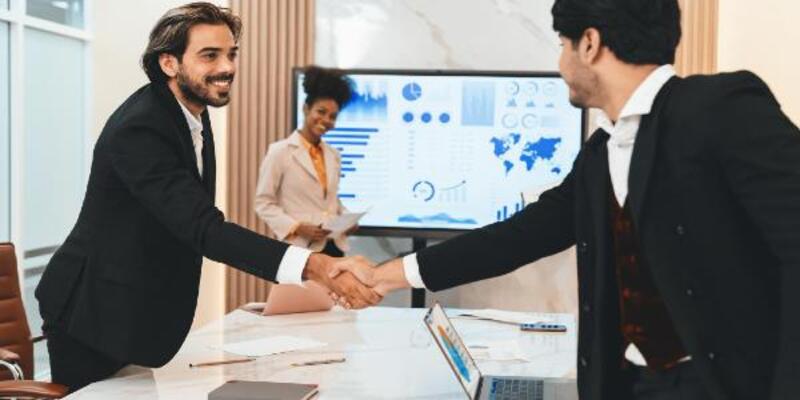 Successful smiling businesspeople shaking hands while making agreement on table with document