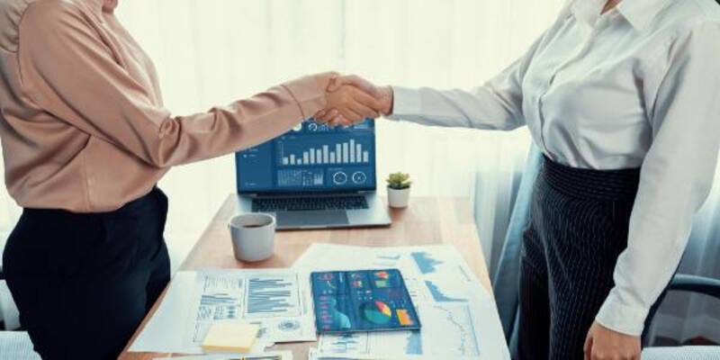 Two asian businesswomen handshake in modern office with data paper enthusiastic