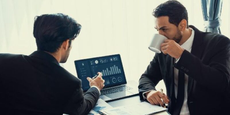 Two men sitting at a desk, one of them is looking at a screen showing a graph