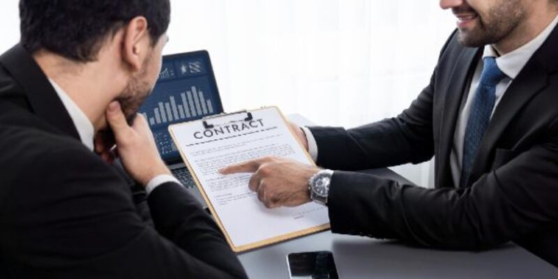 A man is pointing at a contract on a clipboard