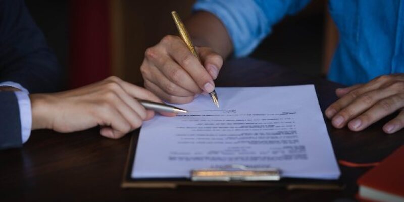 Woman signing while agent pointing on paper in office