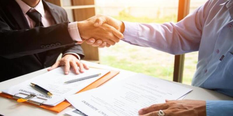 Midsection of lawyer shaking hands with client over table in office