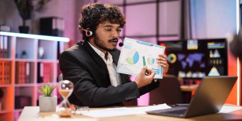 Man holding graphs on a paper in his hand infront of laptop