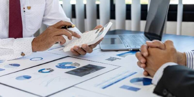 Businessman using white calculator in a business meeting and graphs on table