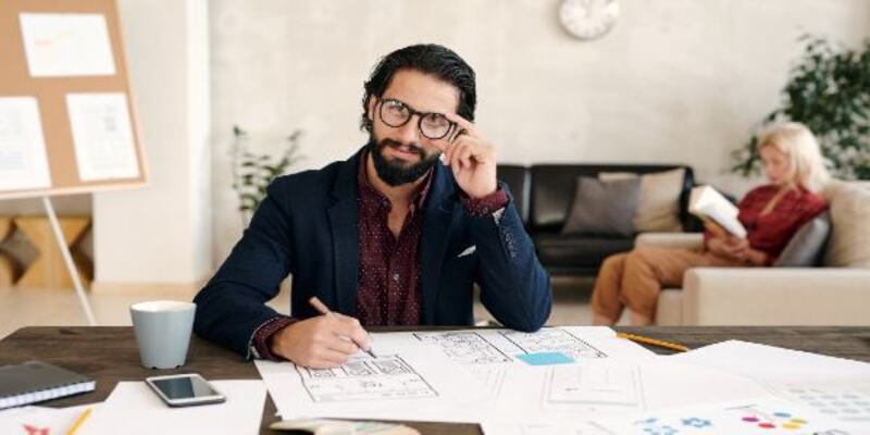 Young bearded successful man holding pencil over paper while working in office