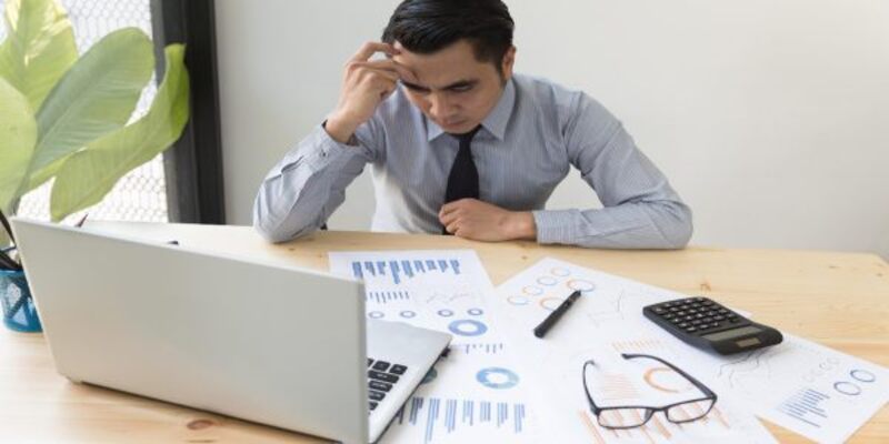 Frustrated man sitting by paper and laptop on table