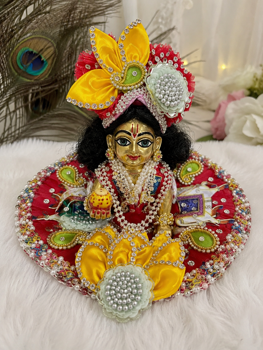 This is a festive yellow and red Laddu Gopal poshak set featuring embroidered cow motifs, a peacock feather accent, and a matching mukut.