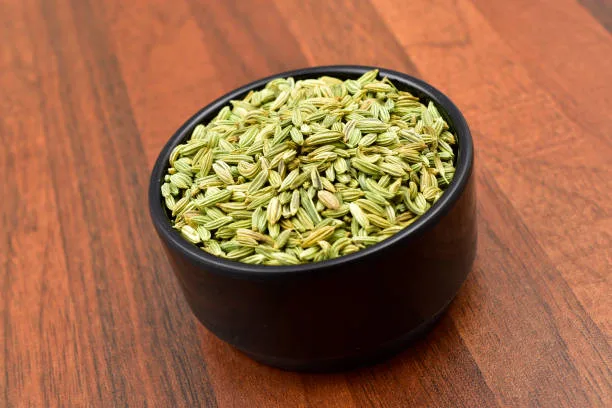 Fennel seeds in a blacl bowl on wooden table.