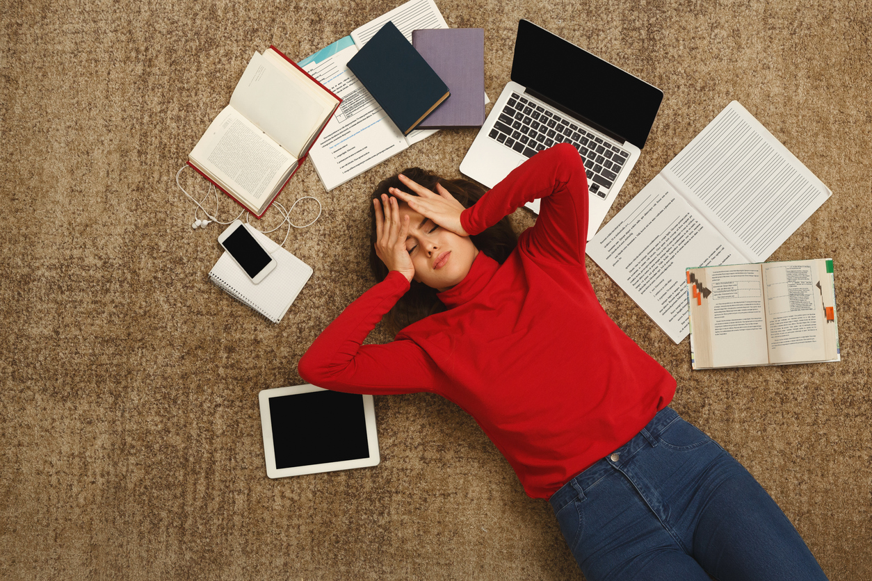Tired student girl lying on the floor with books and gadgets Exam stress