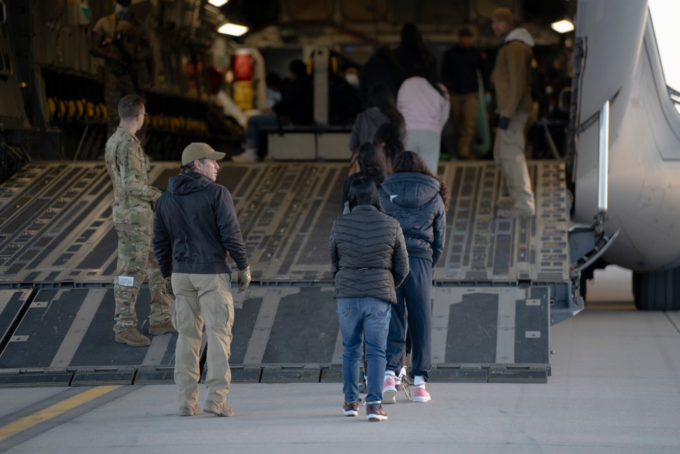 Migrants Alleged illegal migrants, handcuffed and chained, board a USAF aircraft. (X/US Air Force)