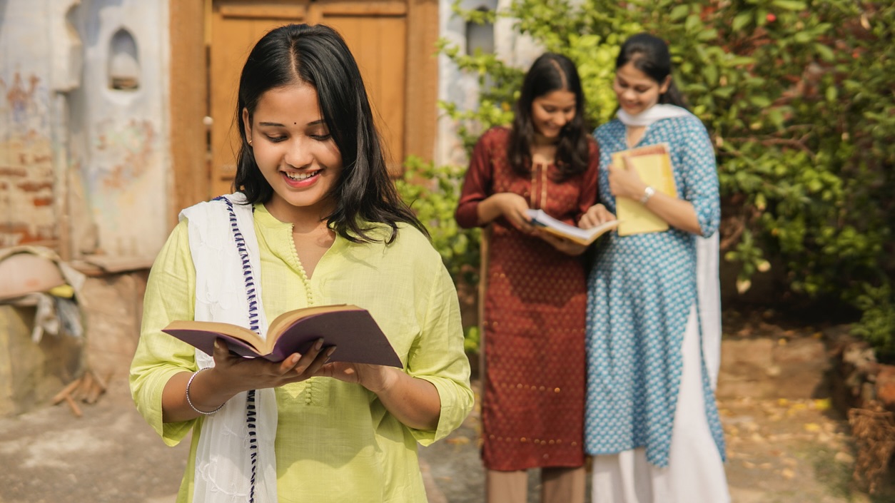 Portrait of cheerful indian female college students reading a book. As female graduation rises, birth rates fall: Kerala and Tamil Nadu lead demographic shift