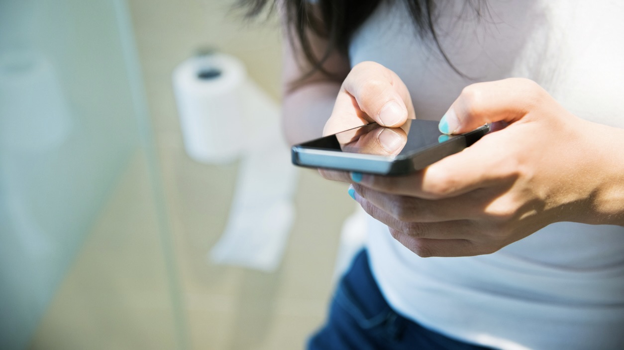 Woman in toilet using smart phone Toilets, even when cleaned regularly, still carry a high load of bacteria.