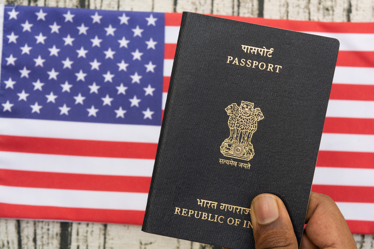 Person holding Indian Passport with hand on a US or american flag as background. H1B visa