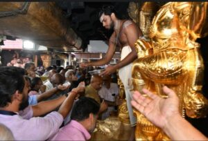 A priest distributing prasadam near to the gold plated Dwarapalaka sculptures at Sabarimala.