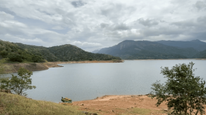 Karaiyar reservoir surrounded by forested hills and mountains under a cloudy sky.