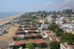 Aerial view of Pattinapakkam showing densely packed homes along the Chennai coastline, with a large modern building marked in the background.