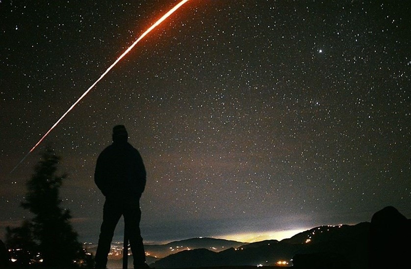 Man standing at the cliff at night gazing at the sky full of starts with houses sparking at night at local uttarakhand village