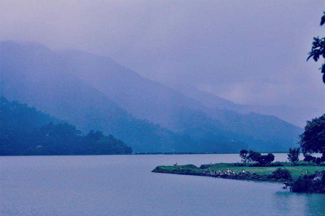 People gathered at the bank of river ganga mesmeriging the view of nature as clouds bursting as they pass through the huge mountain on side of the river