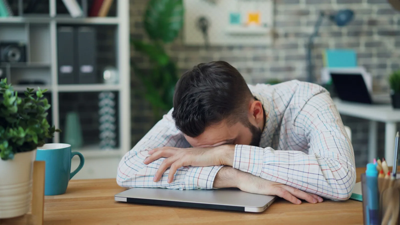 Man asleep with his head on a laptop at a desk